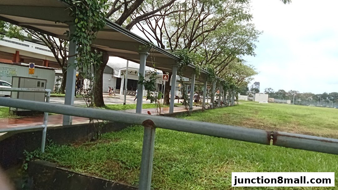 A covered walkway with shops and greenery, leading to a building.