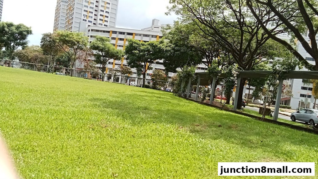 A lush green lawn slopes upwards towards apartment buildings and trees.