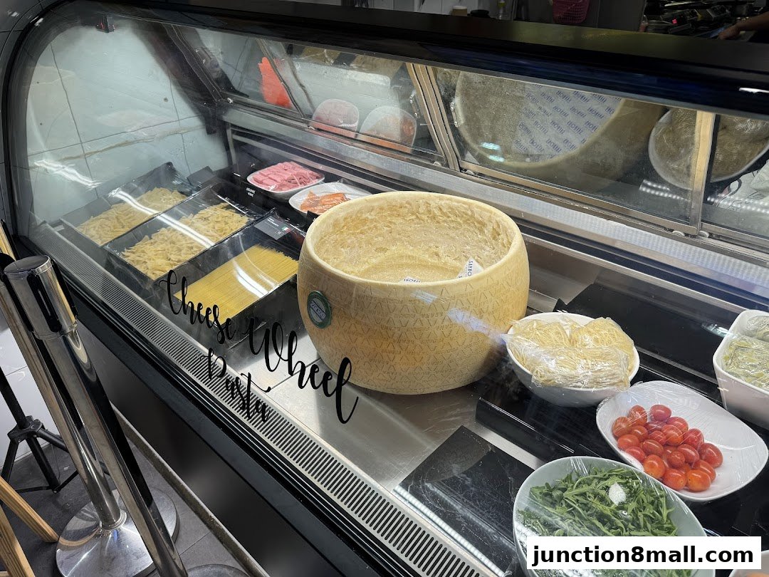 A display case filled with pasta, cheese wheel, tomatoes, and greens at Saybons.