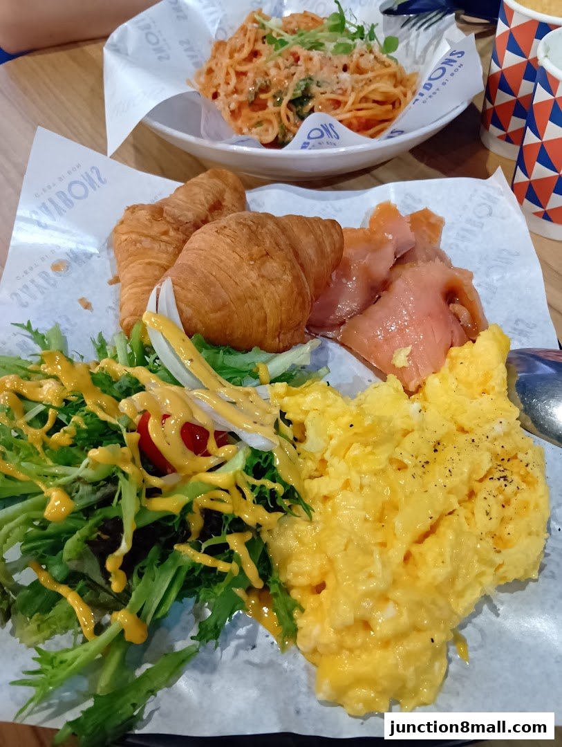 A delicious breakfast spread with scrambled eggs, croissants, smoked salmon, and a fresh salad.
