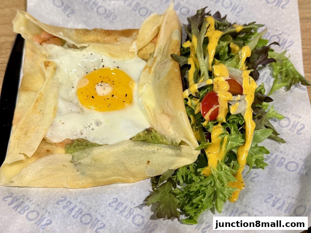 A savory crepe filled with avocado and a fried egg, served with a side salad.