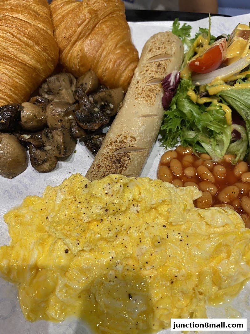 A hearty breakfast platter with scrambled eggs, croissants, sausage, mushrooms, beans, and salad.
