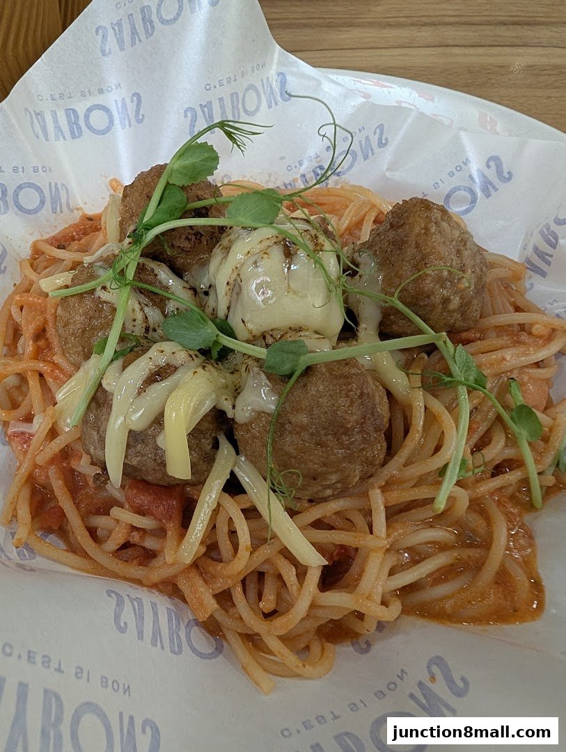 A close-up of spaghetti with meatballs, topped with melted cheese and microgreens.