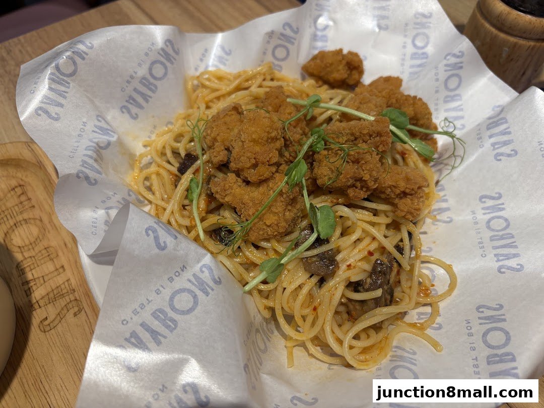 A close-up of a delicious pasta dish with crispy fried chicken pieces and microgreens.