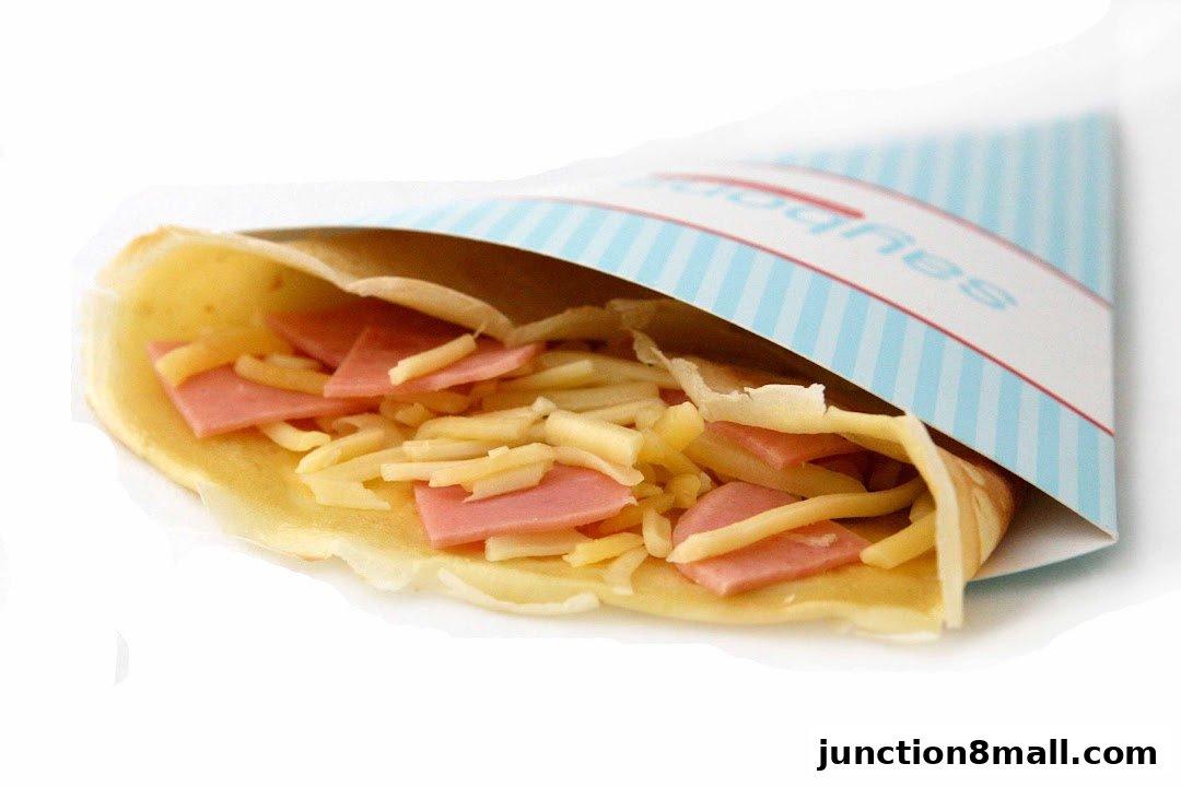 A close-up of a savory crepe filled with ham and cheese, served in branded packaging.