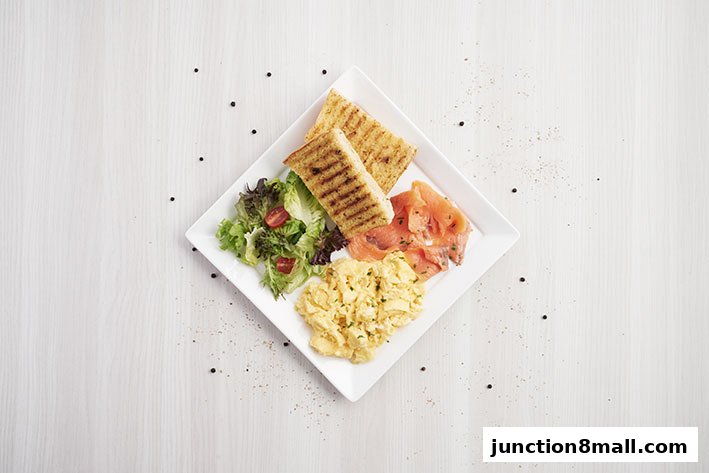A delicious breakfast plate with scrambled eggs, smoked salmon, toast, and a side salad.