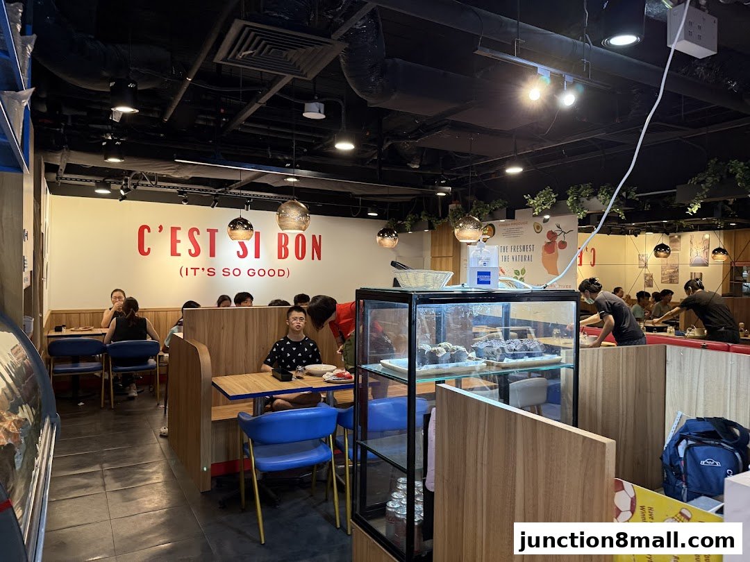 Interior of a restaurant with customers seated at tables and a display case with food.
