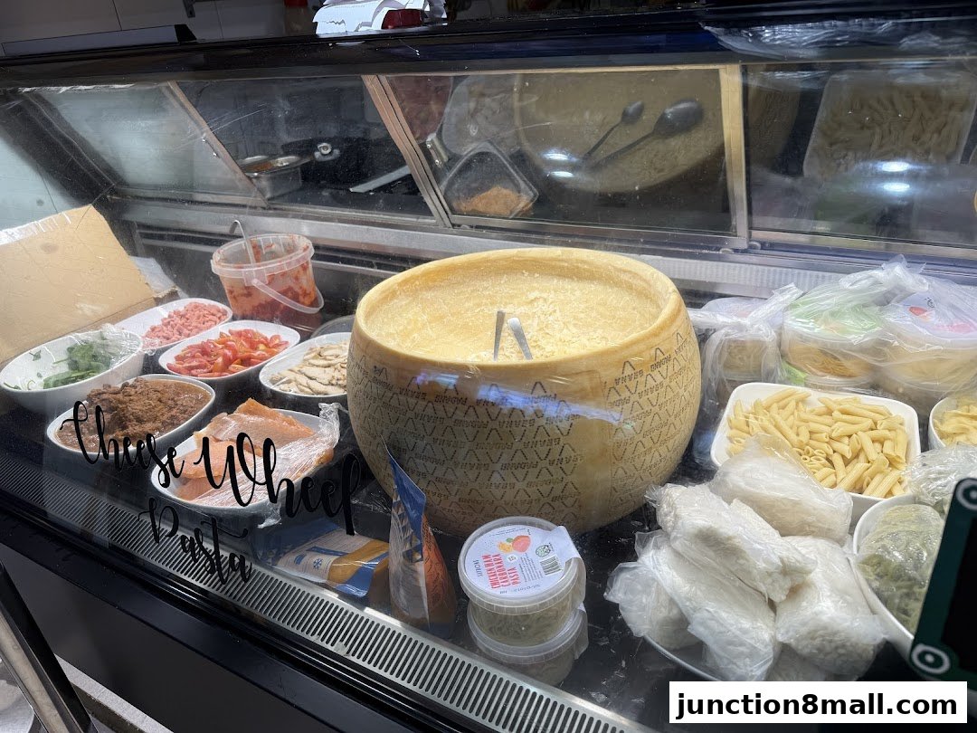 A display case filled with fresh ingredients including a large cheese wheel, pasta, and various toppings.