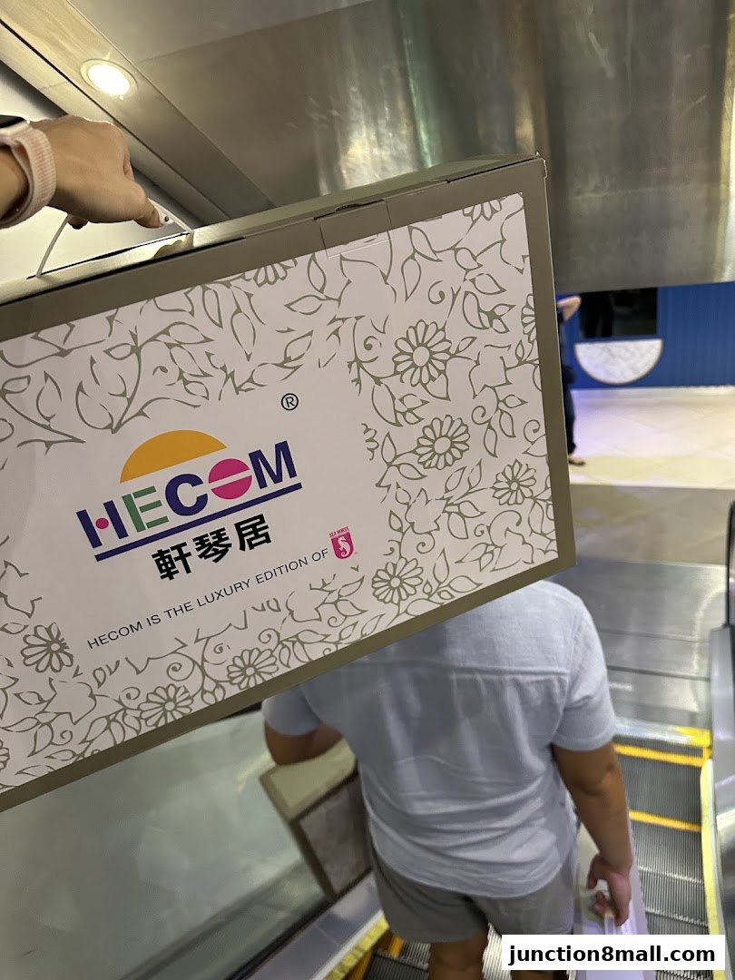 A person carries a box with the HECOM logo and floral design on an escalator.