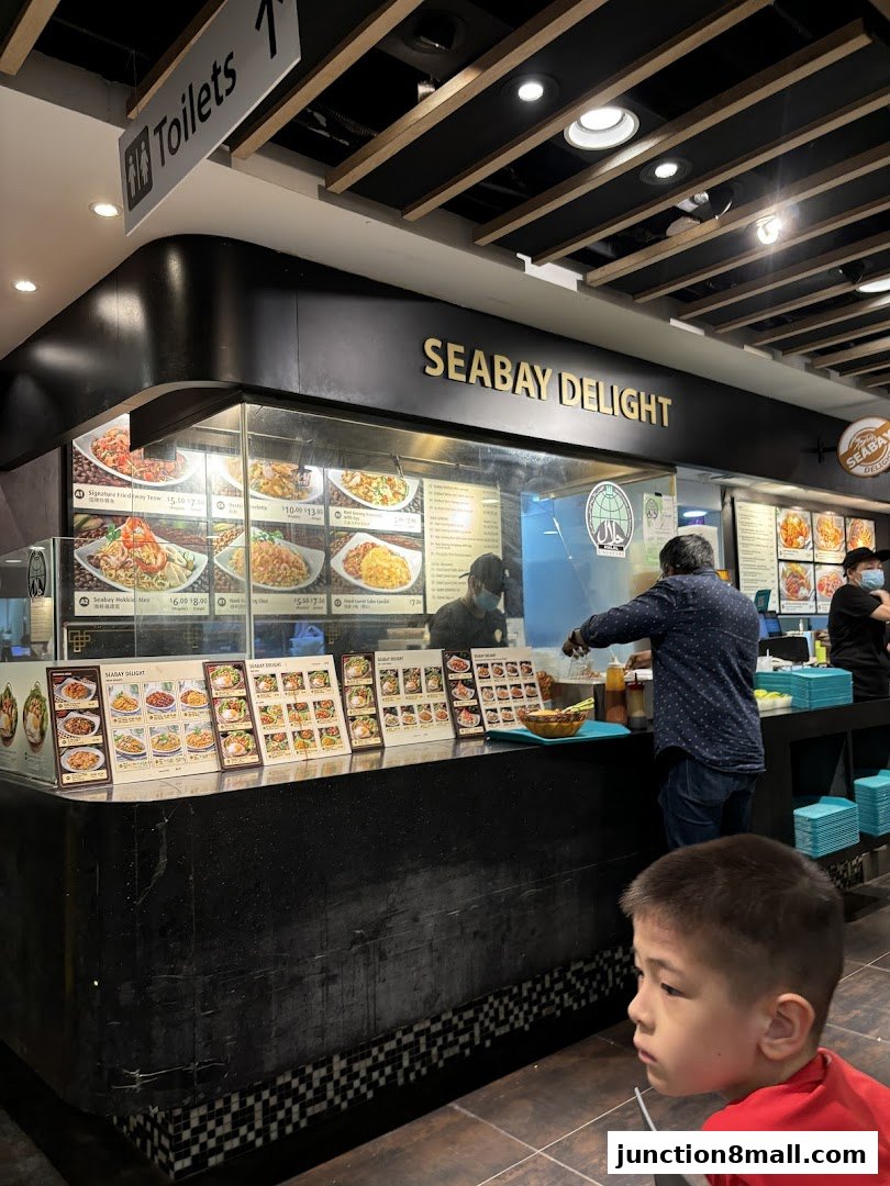 A food stall named Seabay Delight with displayed menus and staff serving customers.