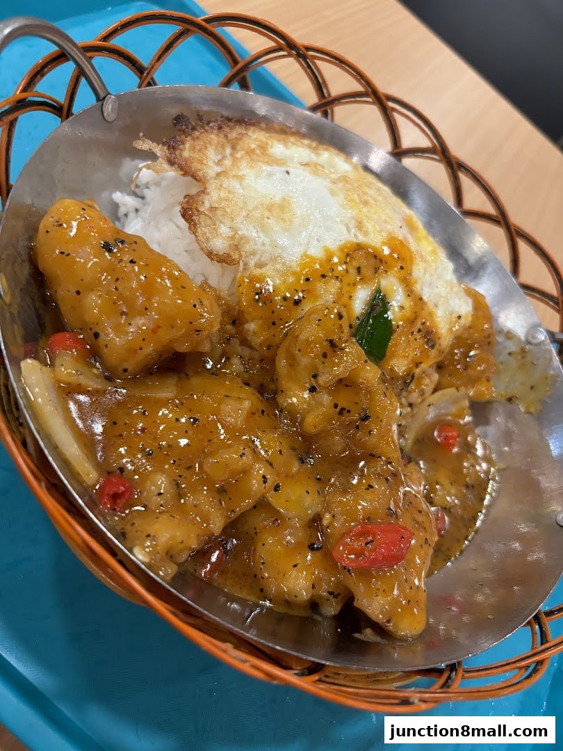 A close-up of a delicious meal featuring rice, a fried egg, and savory chicken in a rich sauce.