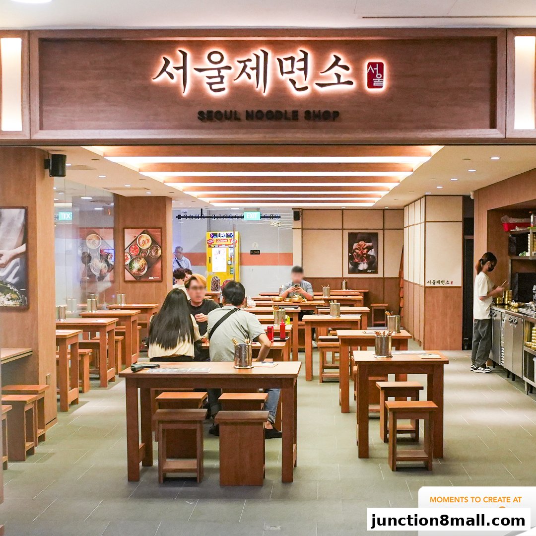The interior of Seoul Noodle Shop with wooden tables and chairs, and a prominent sign.