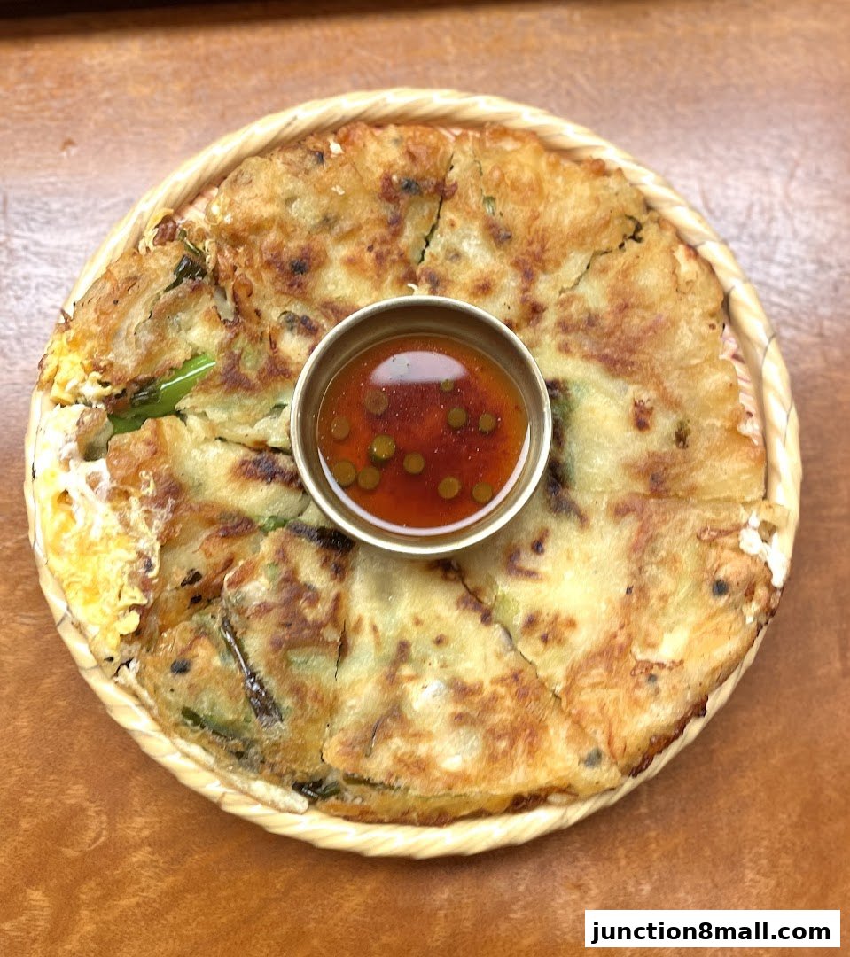 A close-up shot of a savory Korean pancake with a dipping sauce in the center.