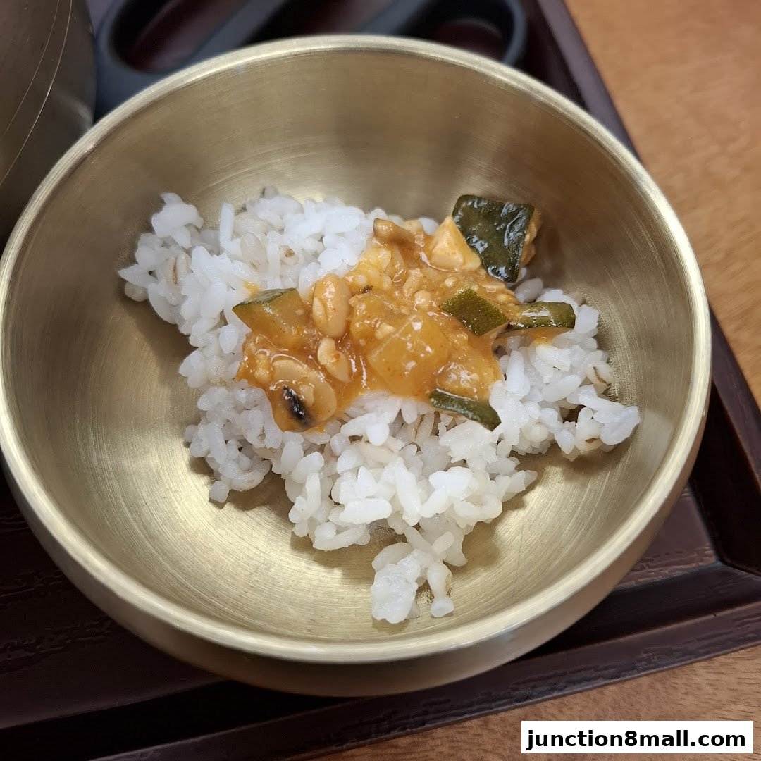 A close-up shot of white rice topped with a savory mixture of vegetables and peanuts in a brass bowl.