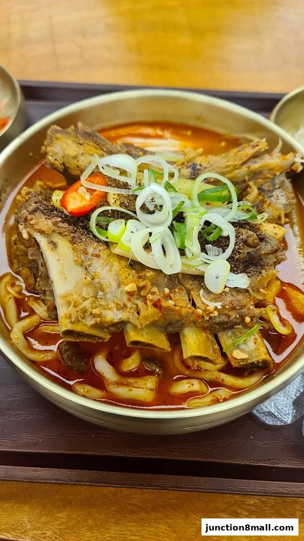 A close-up shot of a steaming bowl of Korean braised short ribs with noodles and garnishes.