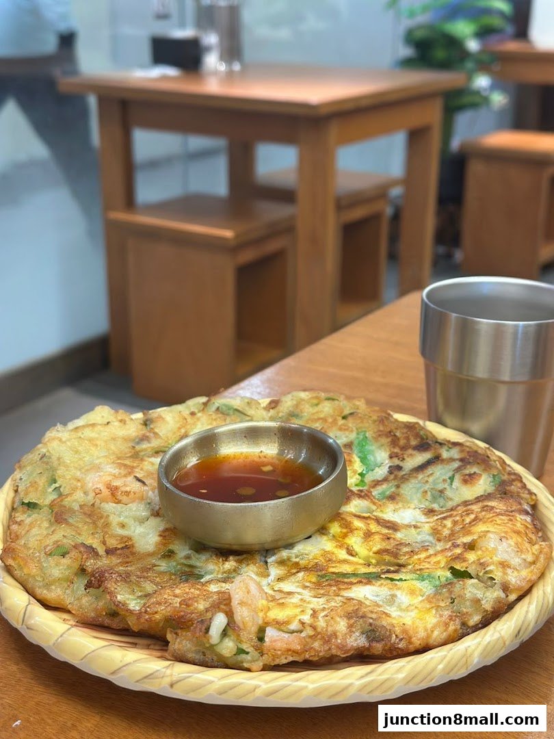 A close-up of a savory Korean pancake with shrimp and scallions, served with dipping sauce.