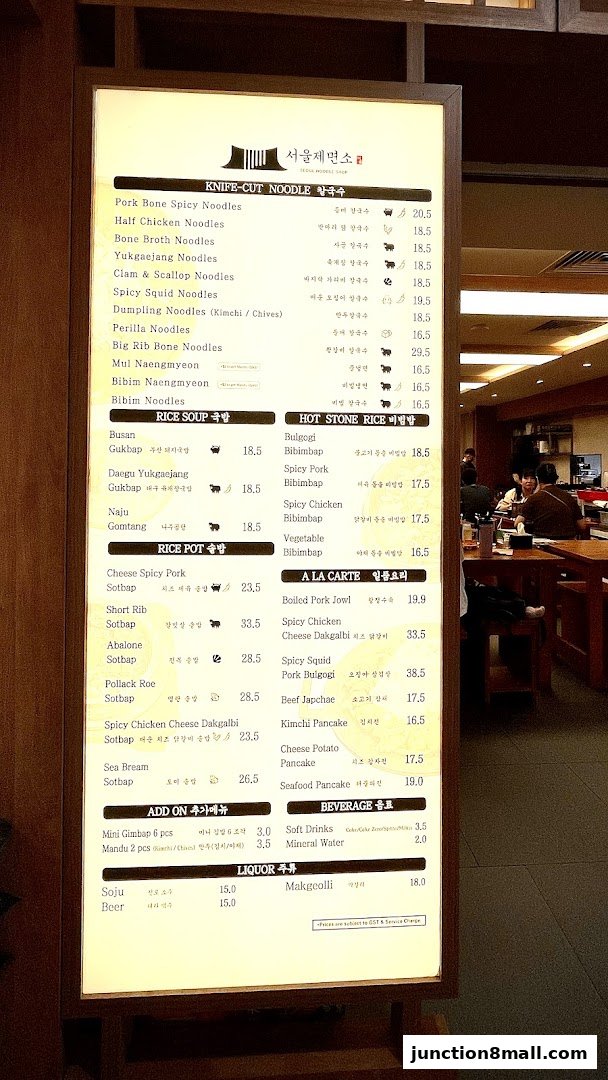 A brightly lit menu board for Seoul Noodle Shop, displaying various Korean dishes and drinks.