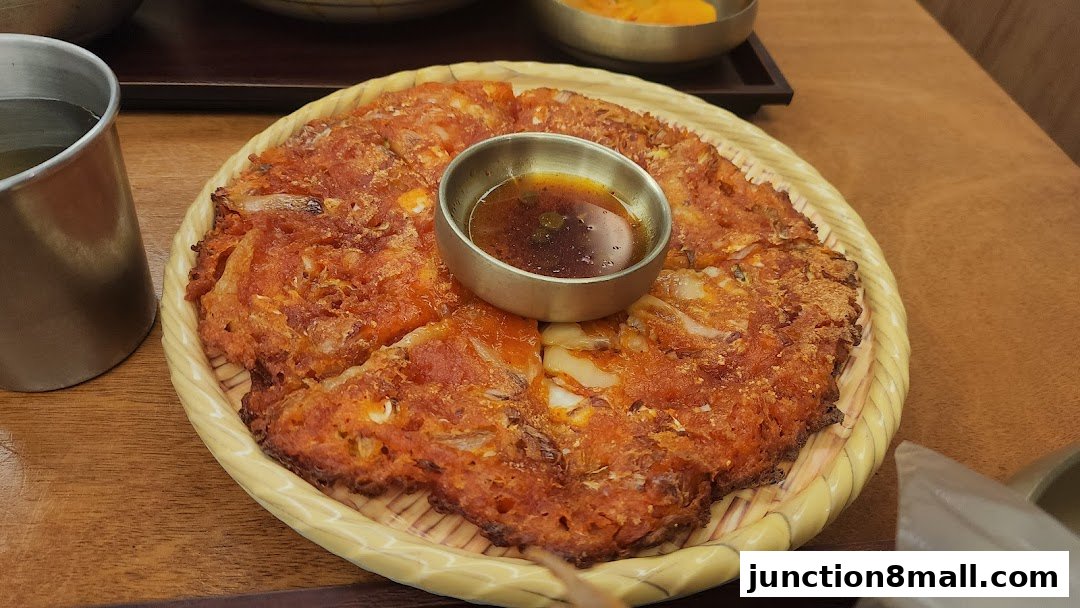 A close-up of a savory Korean pancake with a dipping sauce in the center.