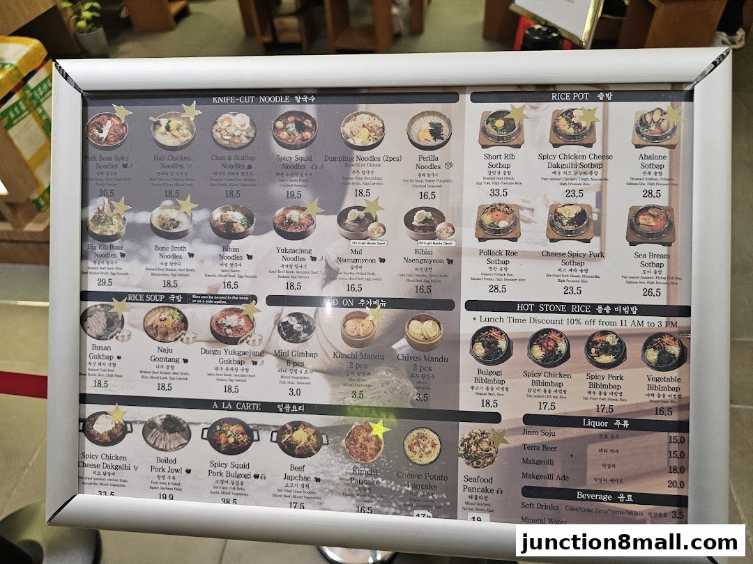 A menu board displaying various Korean noodle dishes, rice pots, soups, and side dishes with prices.