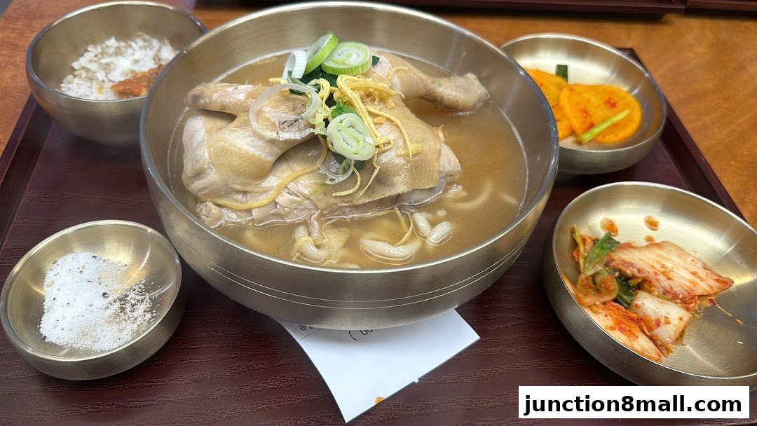 A steaming bowl of Korean chicken soup with rice and kimchi side dishes.