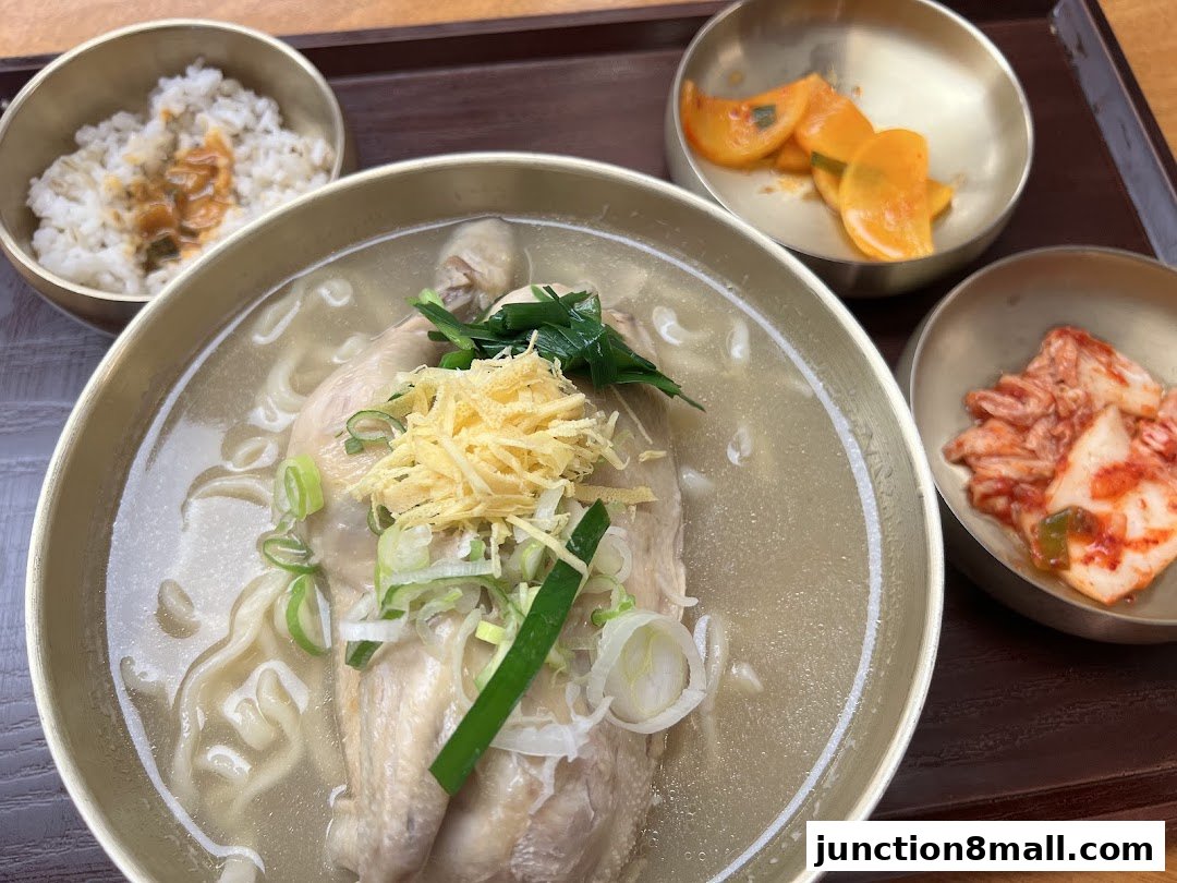 A close-up of a hearty Korean chicken noodle soup with rice and kimchi.