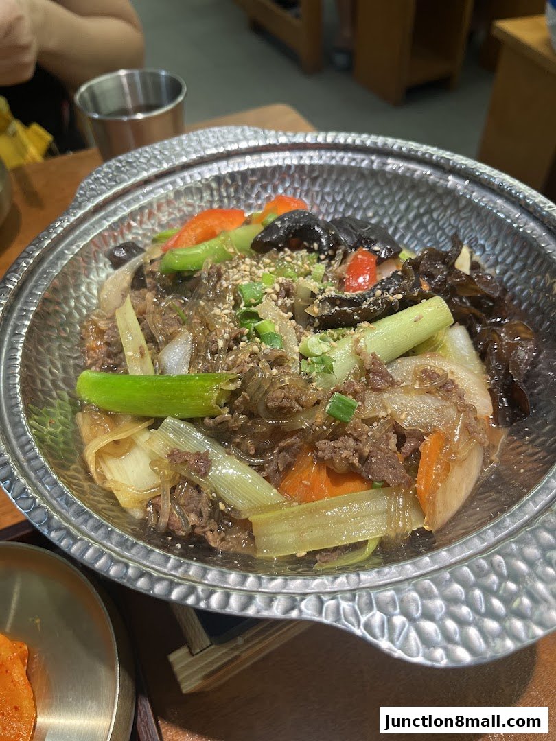 A close-up of a Korean noodle dish with beef, vegetables, and sesame seeds.