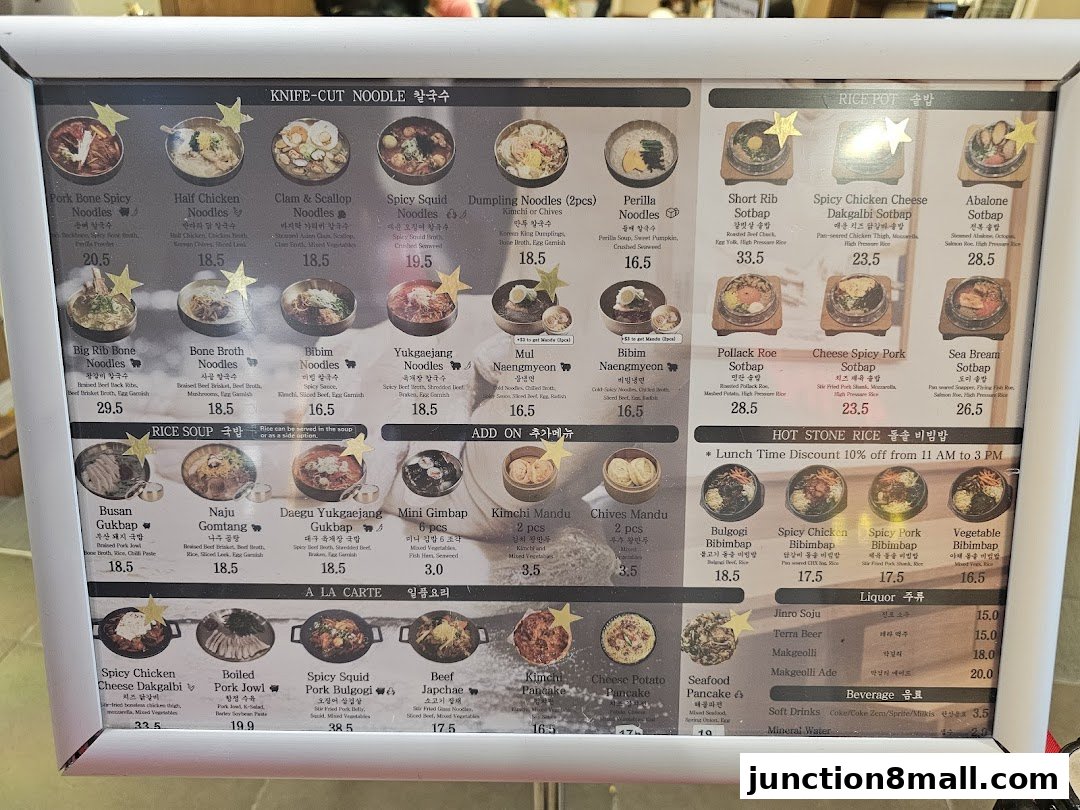 A menu board displaying various Korean noodle dishes, rice pots, soups, and side dishes with prices.