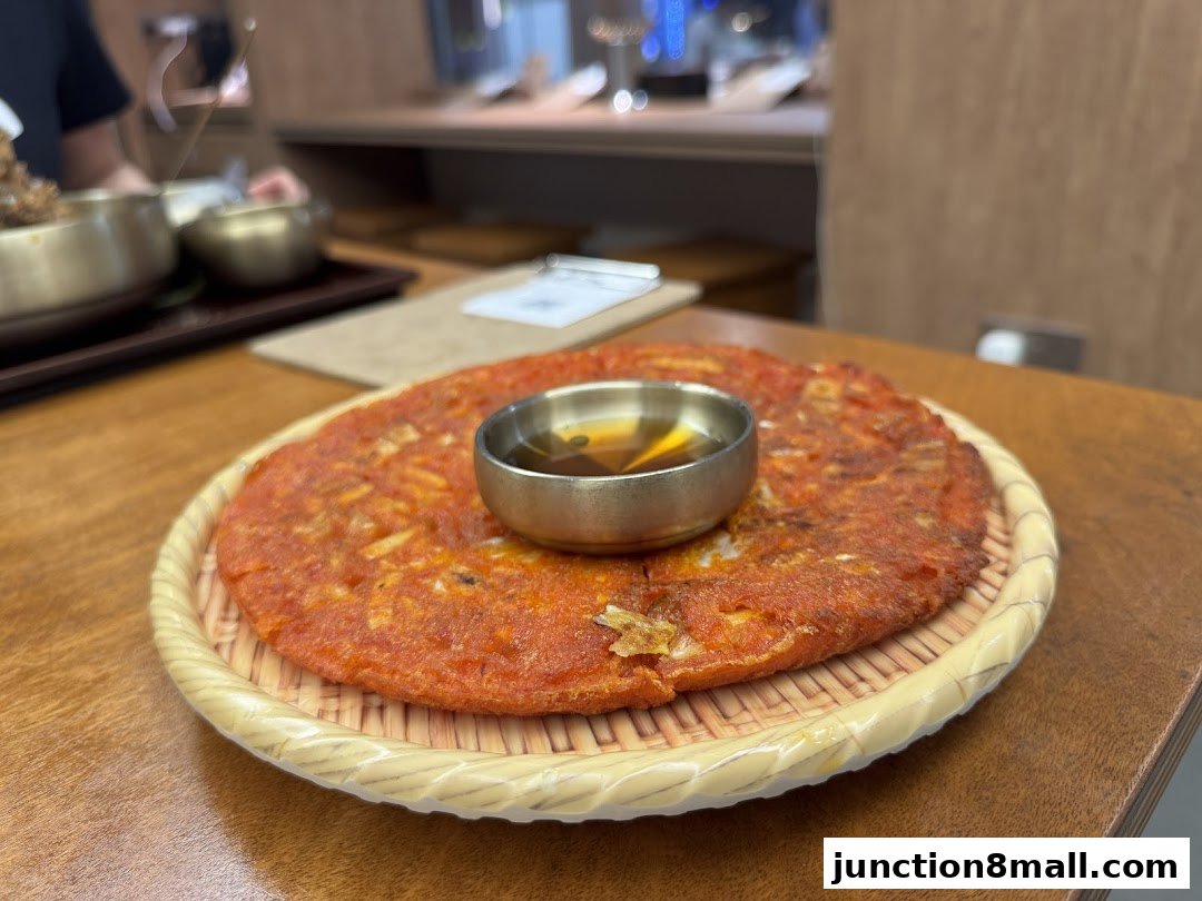 A close-up of a Korean pancake with a dipping sauce in the center.