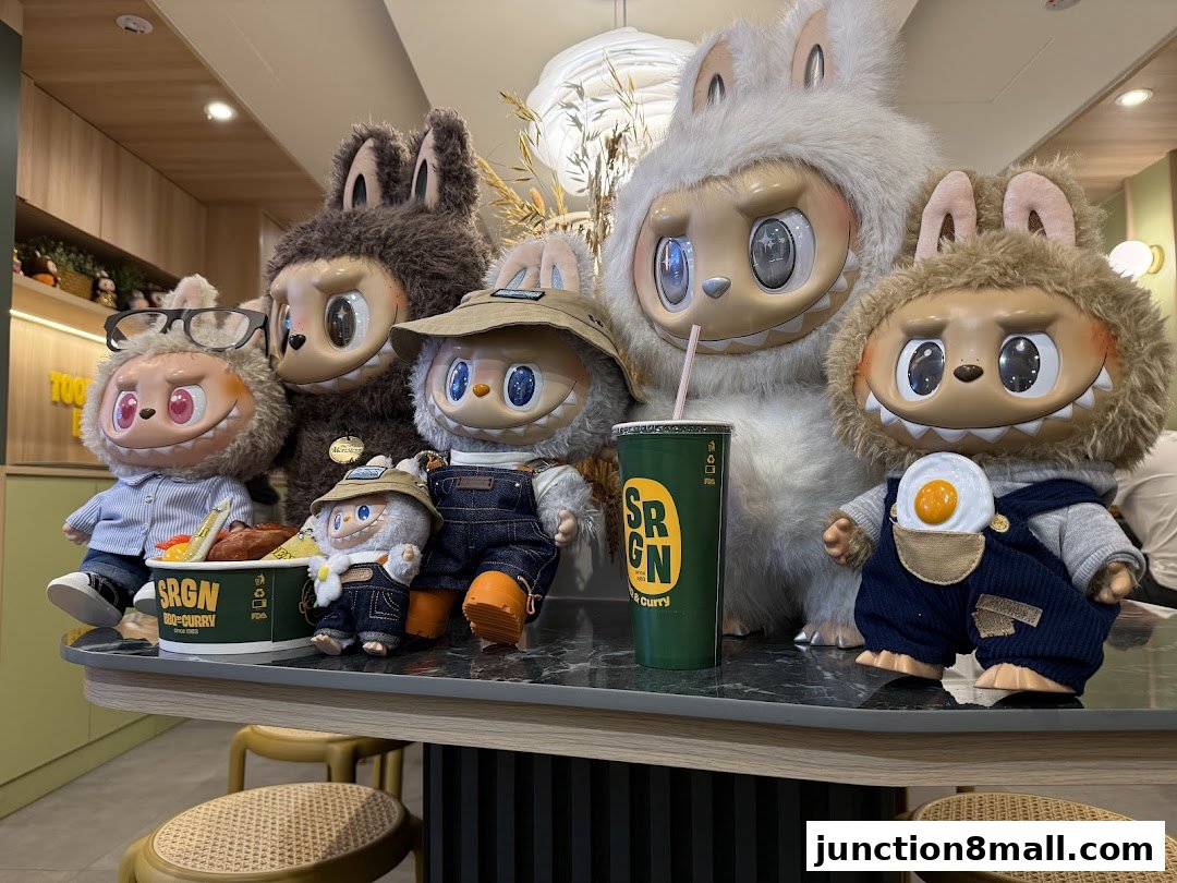 A group of collectible plush toys are displayed on a counter with food and drinks.