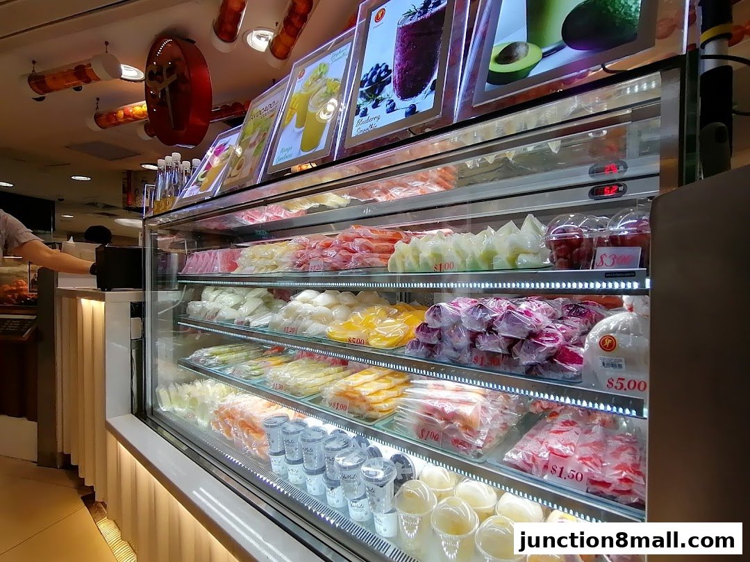 A display fridge filled with fresh fruits and juices, with promotional images at the top.