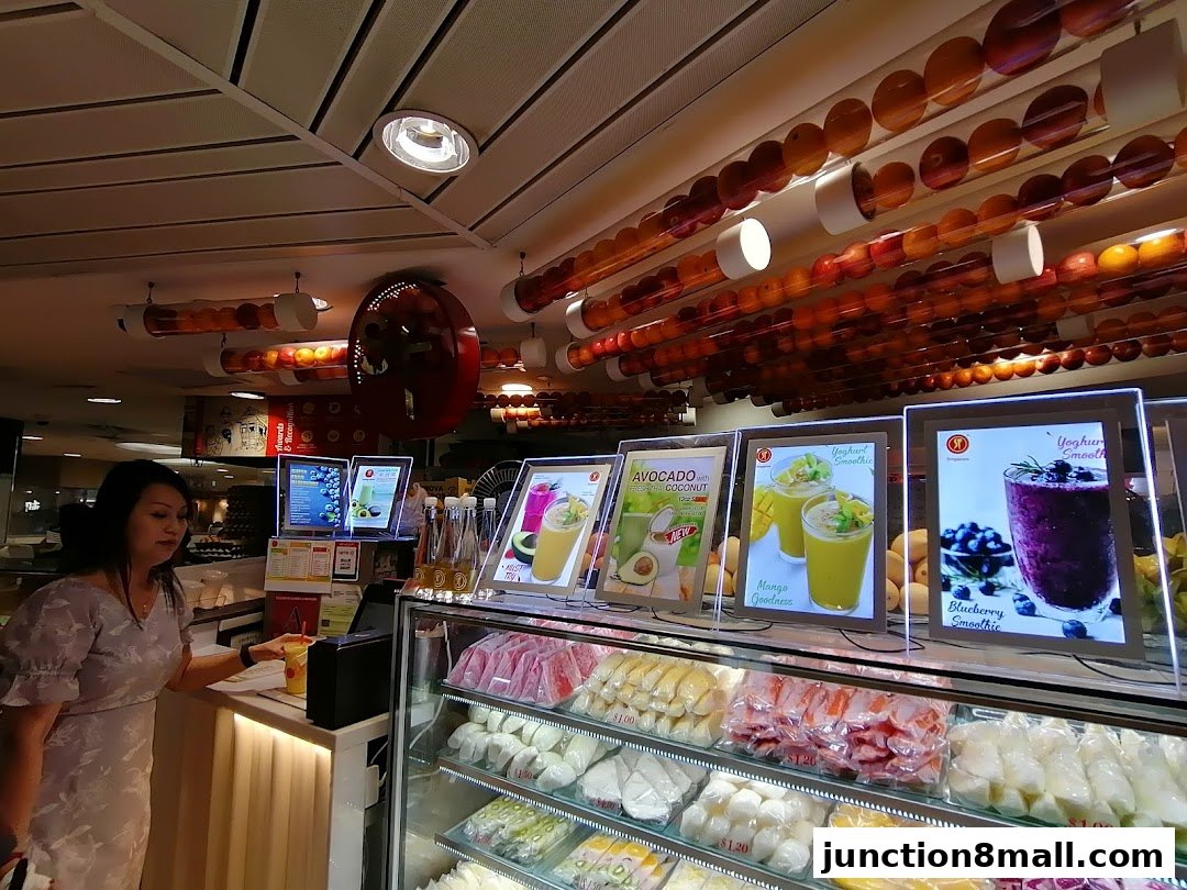 A woman orders a drink at a juice bar with colorful fruit displays and illuminated menu boards.