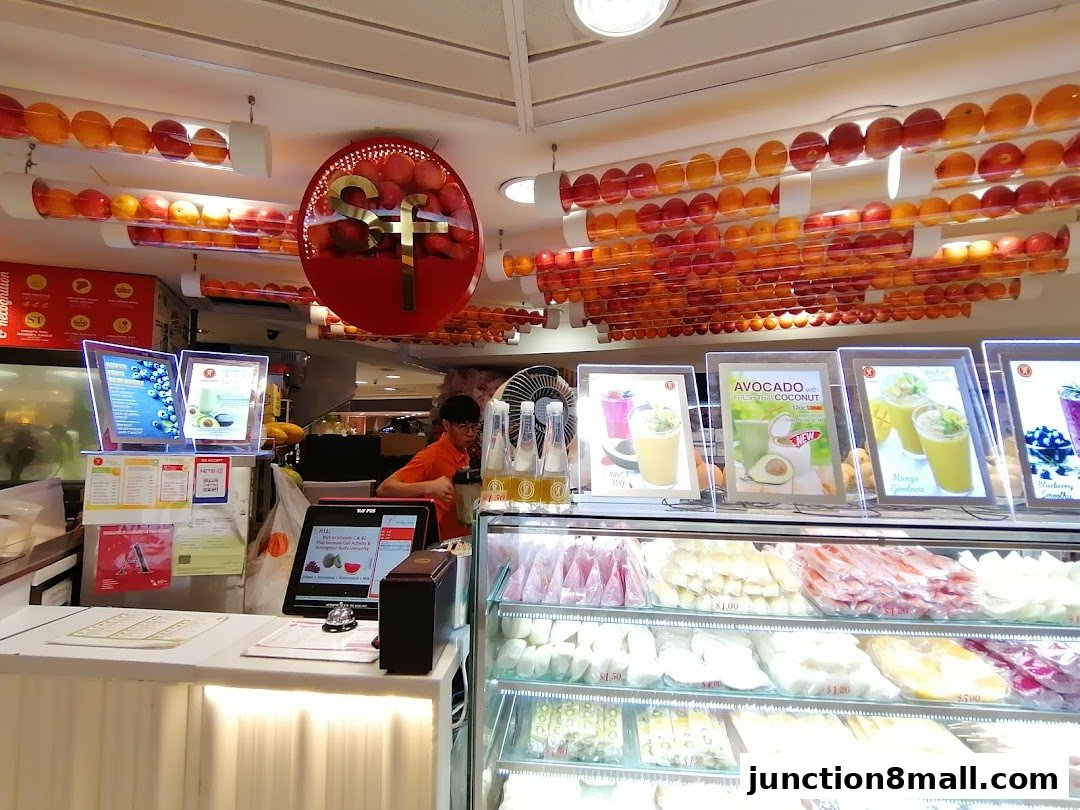 A juice shop counter with illuminated menu displays and a variety of fresh fruits.