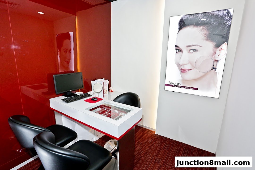A modern beauty treatment room with a desk, computer, chairs, and a large advertisement.