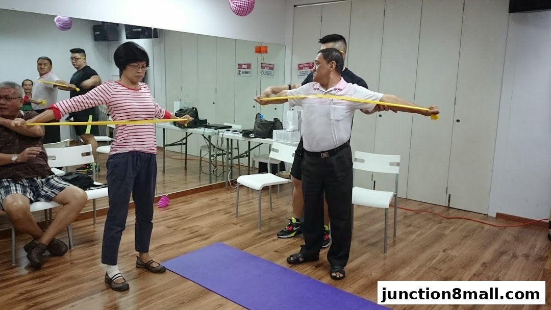 People exercising with resistance bands in a room with mirrors and chairs.