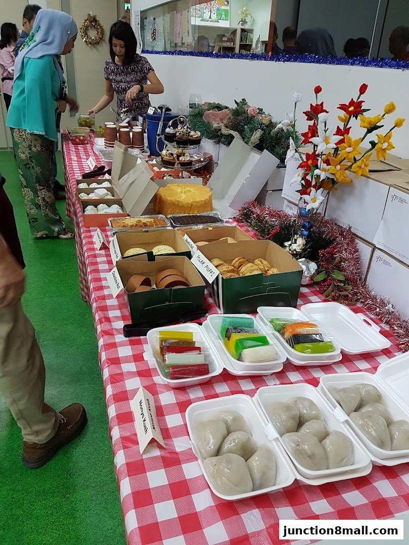 A table laden with various desserts and pastries, including cupcakes, cakes, and colorful kueh.