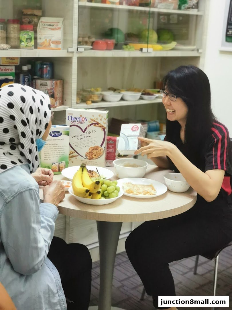 Two women are sitting at a table with healthy food options and products on display.