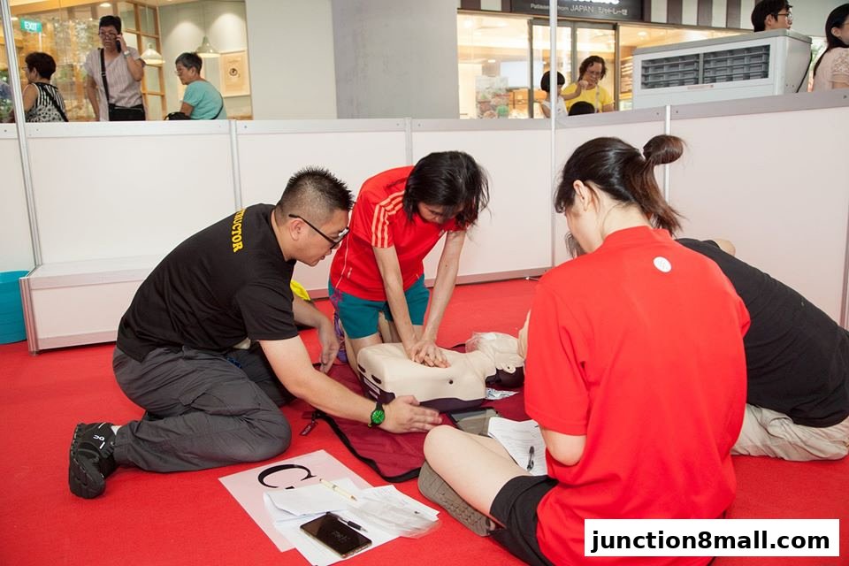 People practicing CPR on a dummy during a health and wellness event.