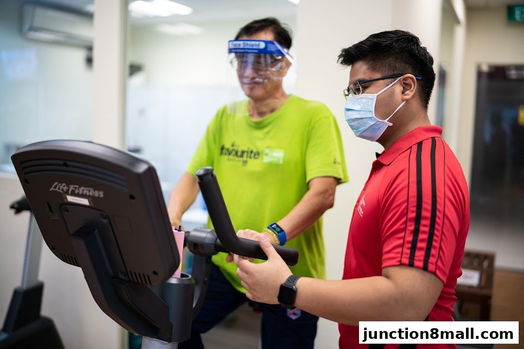 A physiotherapist assists an elderly man on an exercise bike at a wellness center.