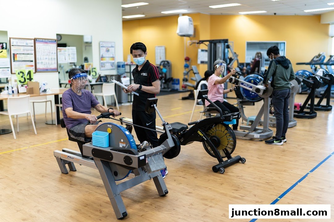 People exercising on rowing machines with a trainer overseeing.