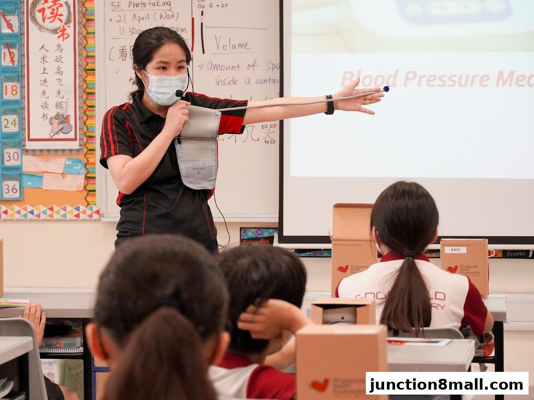 A woman in a mask teaches students about blood pressure measurement using a projector.
