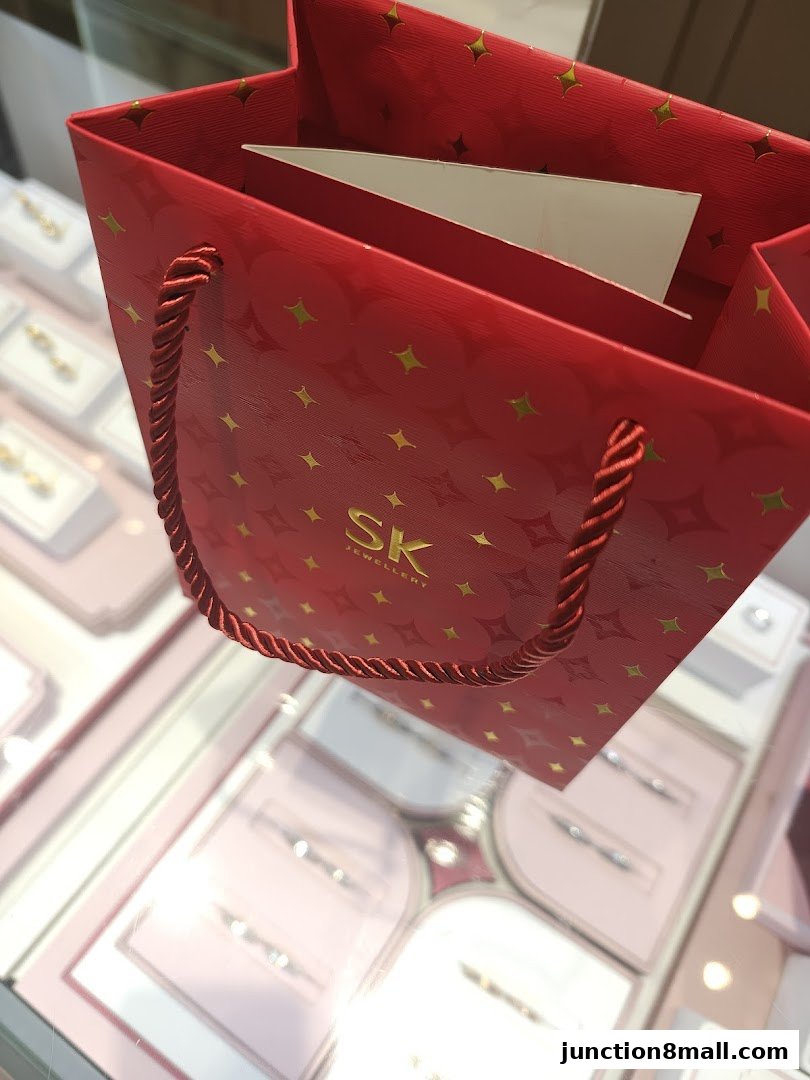 A red SK Jewellery shopping bag with gold star pattern and rope handles.