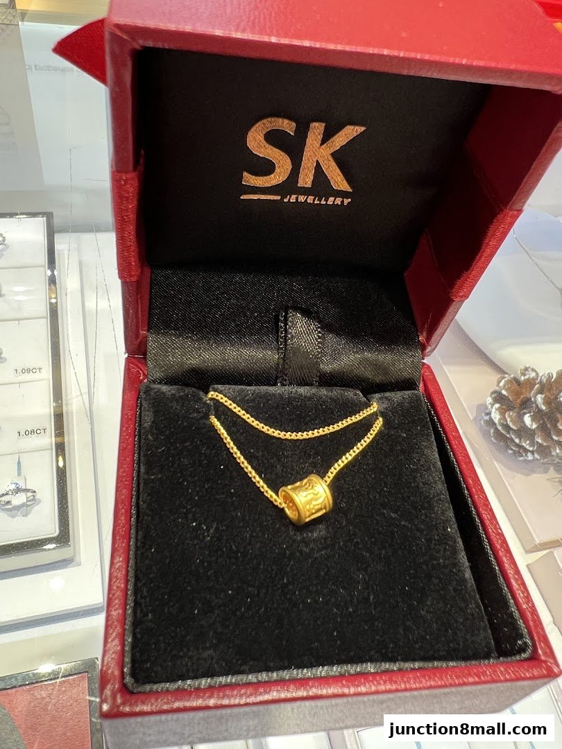 A gold pendant necklace with a cylindrical charm in a red jewelry box.