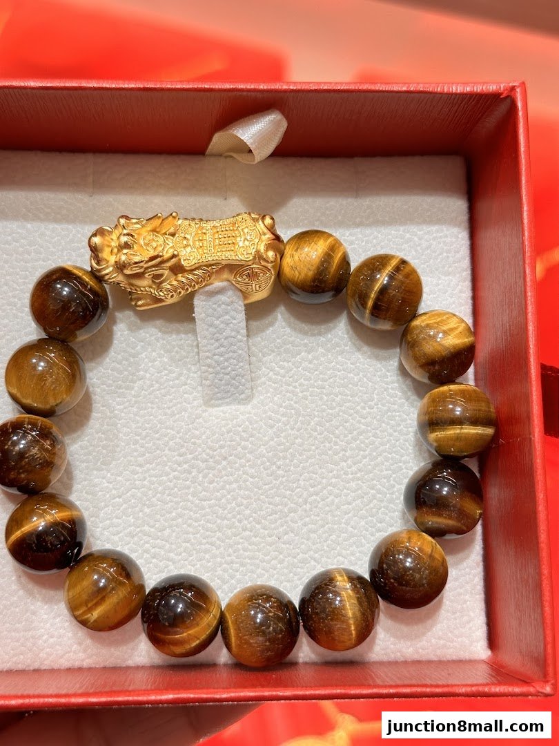 A close-up of a tiger's eye stone bracelet with a gold Pixiu charm in a red box.