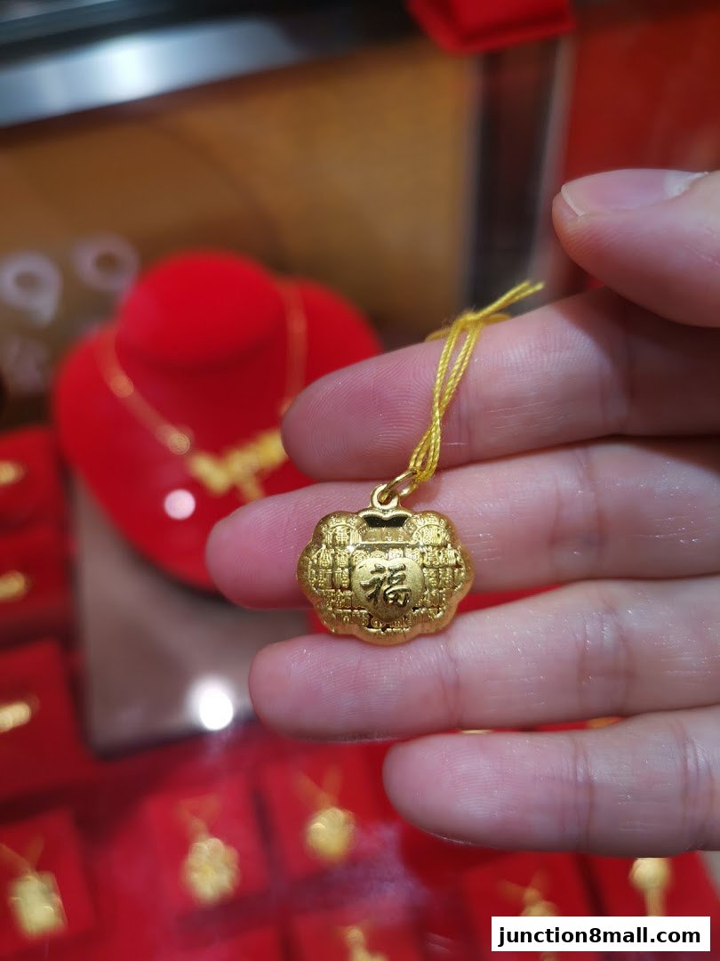 A hand holds a gold pendant with Chinese characters, showcasing jewelry in a store.
