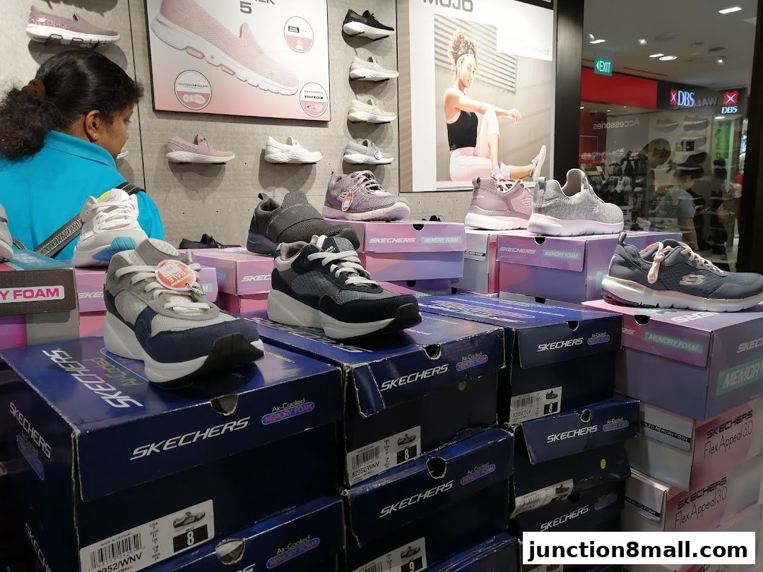 A display of Skechers shoes on boxes, with a customer browsing in the background.