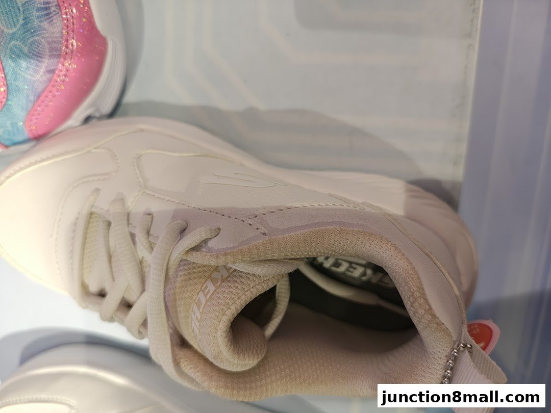 Close-up of white Skechers sneakers with a pink and blue sparkly shoe in the background.