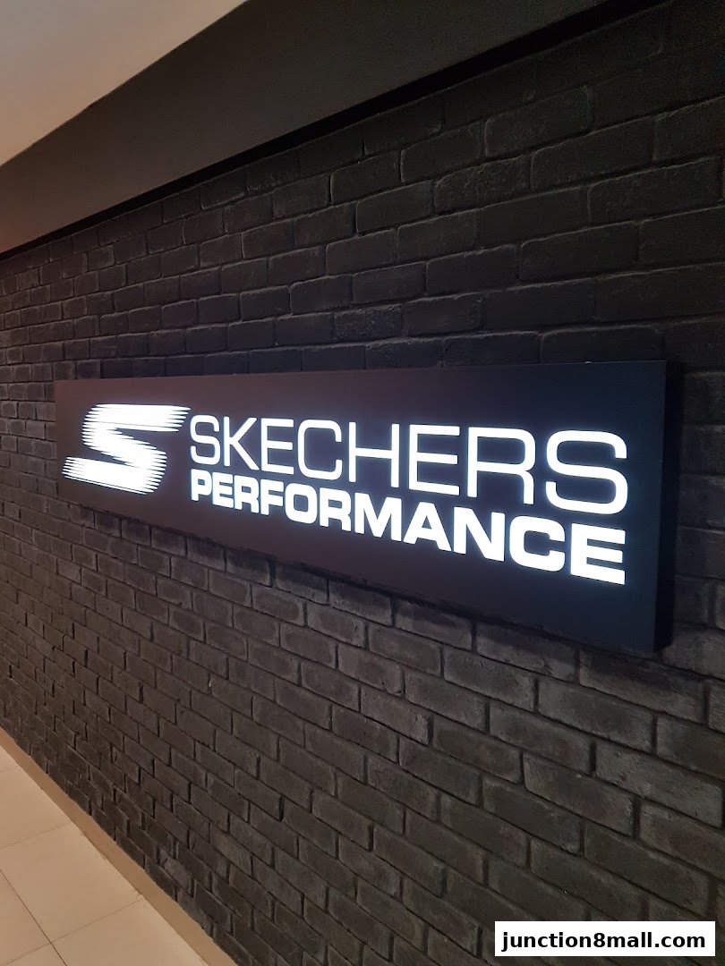 A lit Skechers Performance sign mounted on a dark brick wall.