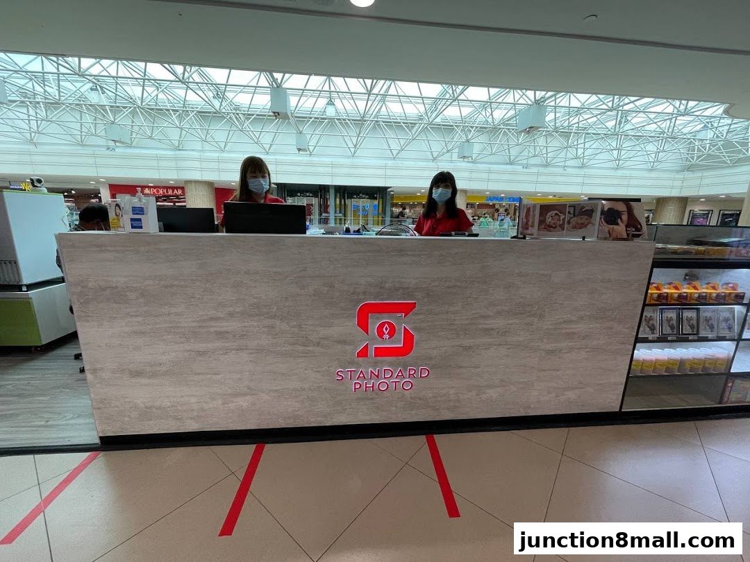Two staff members stand behind a counter at Standard Photo Junction 8, with displays of photos and products.