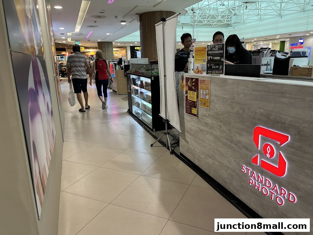 A couple walks past a Standard Photo shop counter with staff serving customers.
