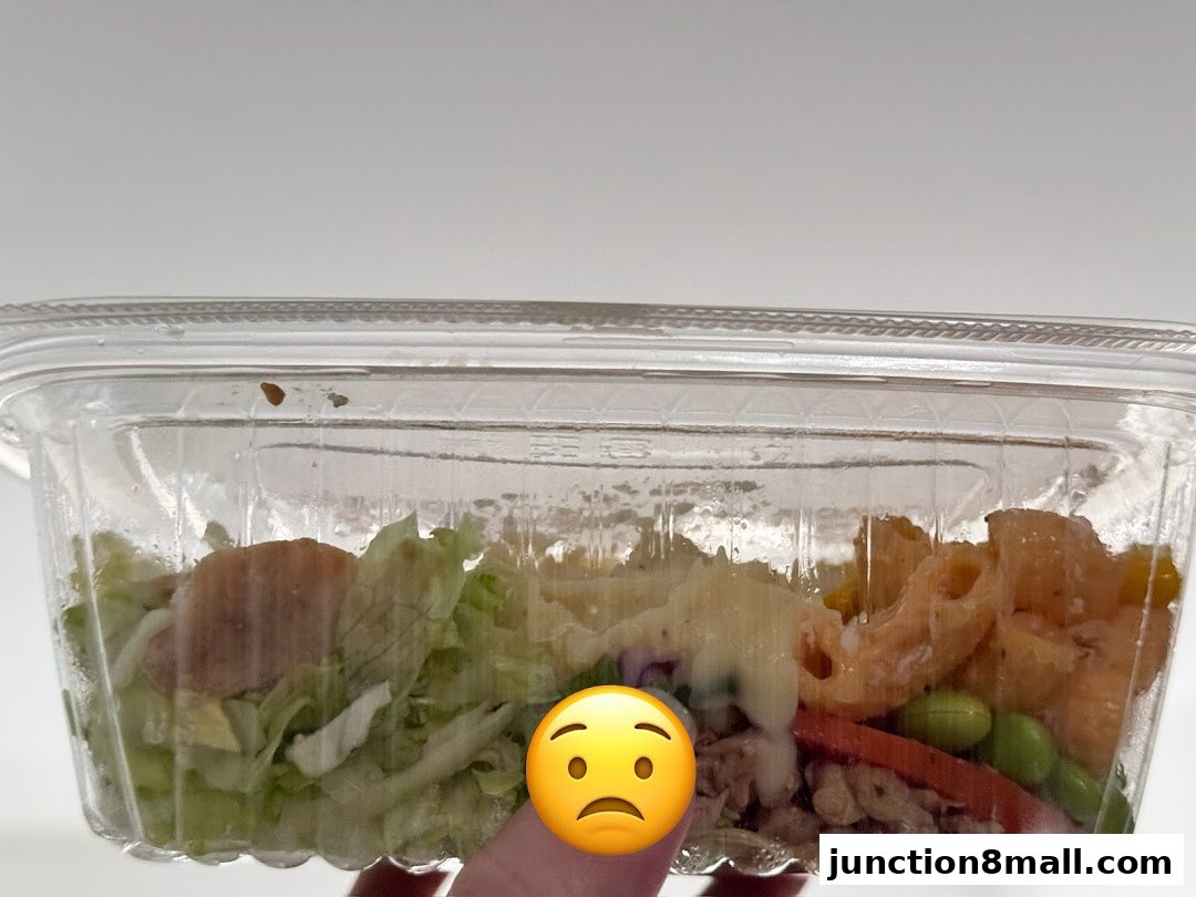 A clear plastic container filled with a salad featuring lettuce, pasta, edamame, and other ingredients.